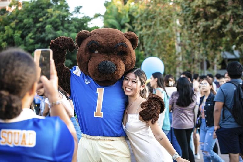 Joe Bruin flexing and posing for a picture with a student