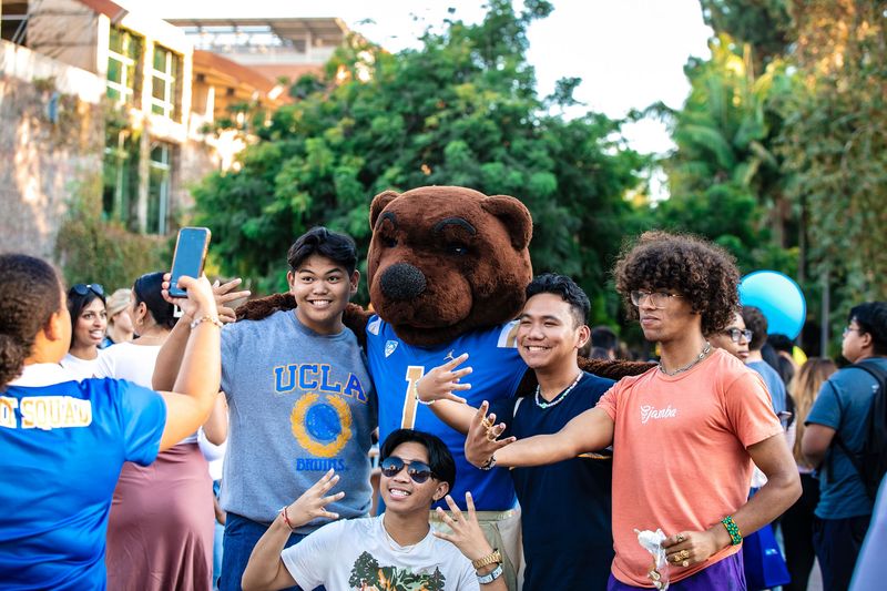 Joe Bruin posing with students for a photo