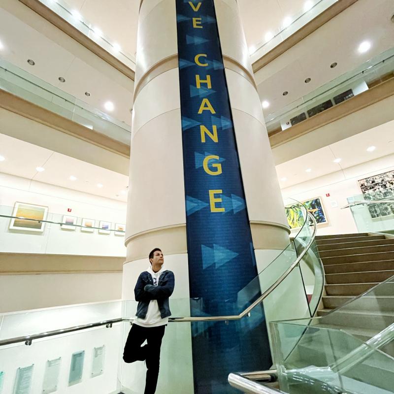 Image of a student standing in front of a pole that has a panel stating, "Drive Change"